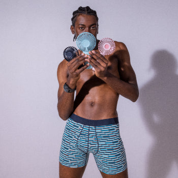 Shirtless man in blue boxer briefs holding three personal fans