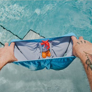 Man holding blue swim shorts overtop of pool with oranges inside interior pouch