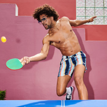 Shirtless man in striped bathing suit playing ping pong