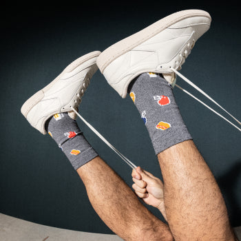 Man in white shoes and grey socks kicking feet in air with laces dangling