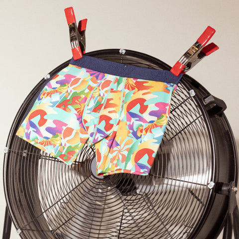 A pair of cooling boxer briefs in a vibrant tropical print clipped to a fan and fluttering