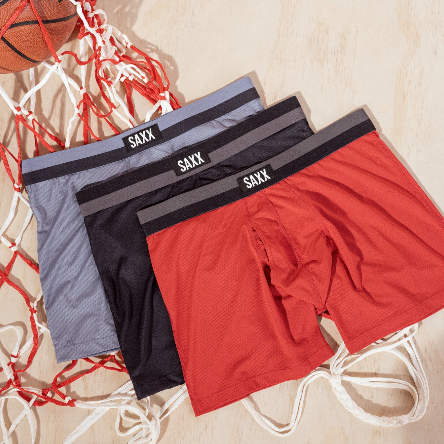 Three pairs of boxer briefs laid on top of a basketball net. The pairs are ordered in red, black, and light blue colors.