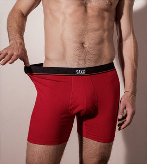 A close-up image of a man wearing a pair of red boxer briefs. He is extending the waist band outwards to the left side of the image.  