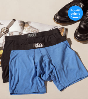 Two pairs of boxer briefs are laid on top of each other on an open magazine. One pair is bright blue, the one underneath the blue pair is black. 