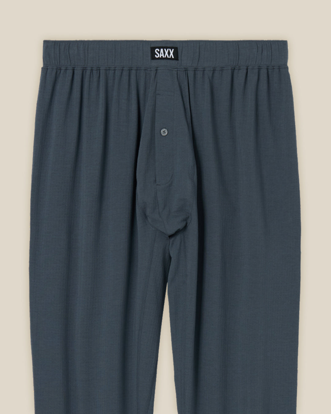 Blue satin pajama pants with SAXX branding on a beige background