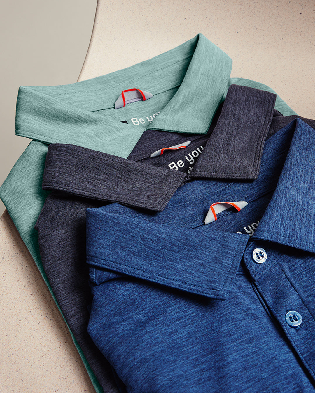 Folded shirts in green, black, and blue with a visible brand logo on a beige background