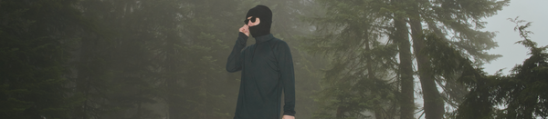 Man in black long sleeve shirt and balaclava standing in snowy woods