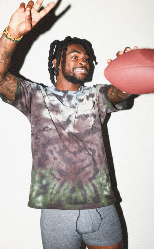 Trevon Diggs smiling while holding up a football and a peace sign in the Vibe Super Soft Boxer Brief in Graphite Heather