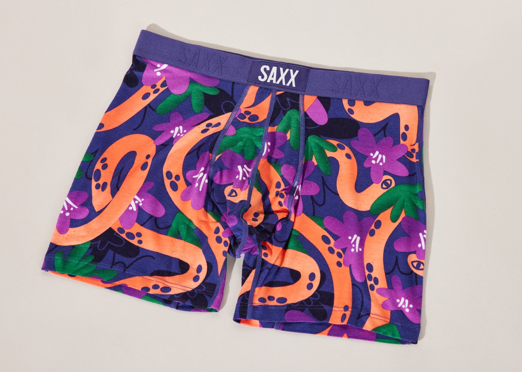 A pair of purple boxer briefs with an orange snake illustrated print. They are flat against a cream background.