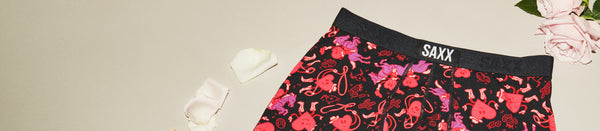 Black underwear with red heart pattern set beside pink rose petals