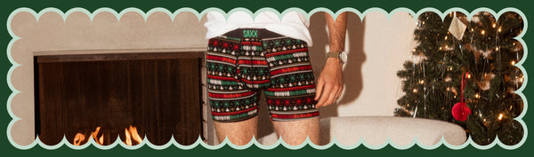 Man wearing a white tee and Boxer Briefs in a holiday print while standing in front of a Christmas tree 