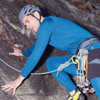 Man rock climbing while wearing blue baselayer top and tights