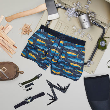 Blue patterned boxer brief surrounded by camping equipment such as axe cooler and tent