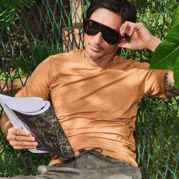 Man in orange shirt and sunglasses reading magazine in hammock