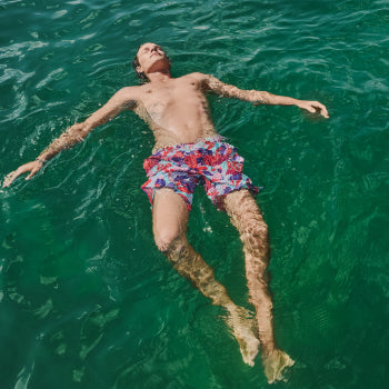 Shirtless man in pink swim shorts floating on top of water