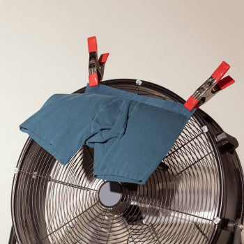 Blue pair of boxer briefs clipped to floor fan blowing in breeze