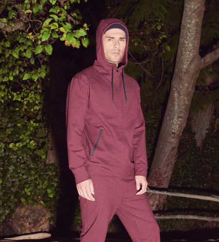 Man in red sweat suit with hood up standing by tree