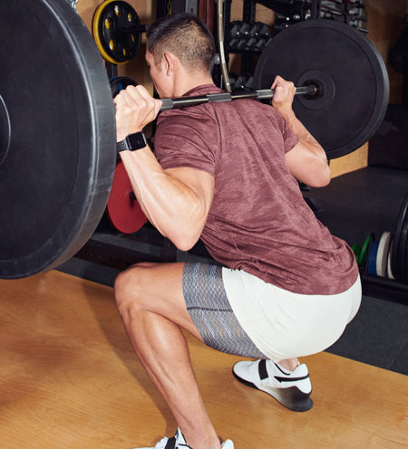 Man wearing white 2N1 Shorts and a maroon tee while doing weighted squats