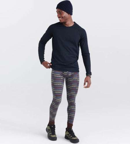 Man in hiking boots wearing a black long sleeve baselayer crew and baselyer tights in a vibrant pattern