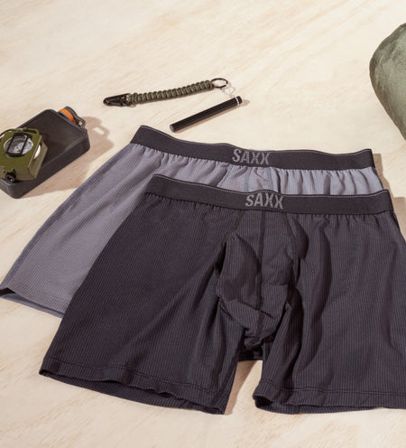 Two pairs of Loose Fit Boxers in gray and black lying next to outdoor adventure supplies