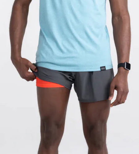 Man wearing gray performance shorts while holding up the leg to show orange liner
