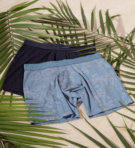 Two pairs of cooling boxer briefs in black and blue on top of palm leaves