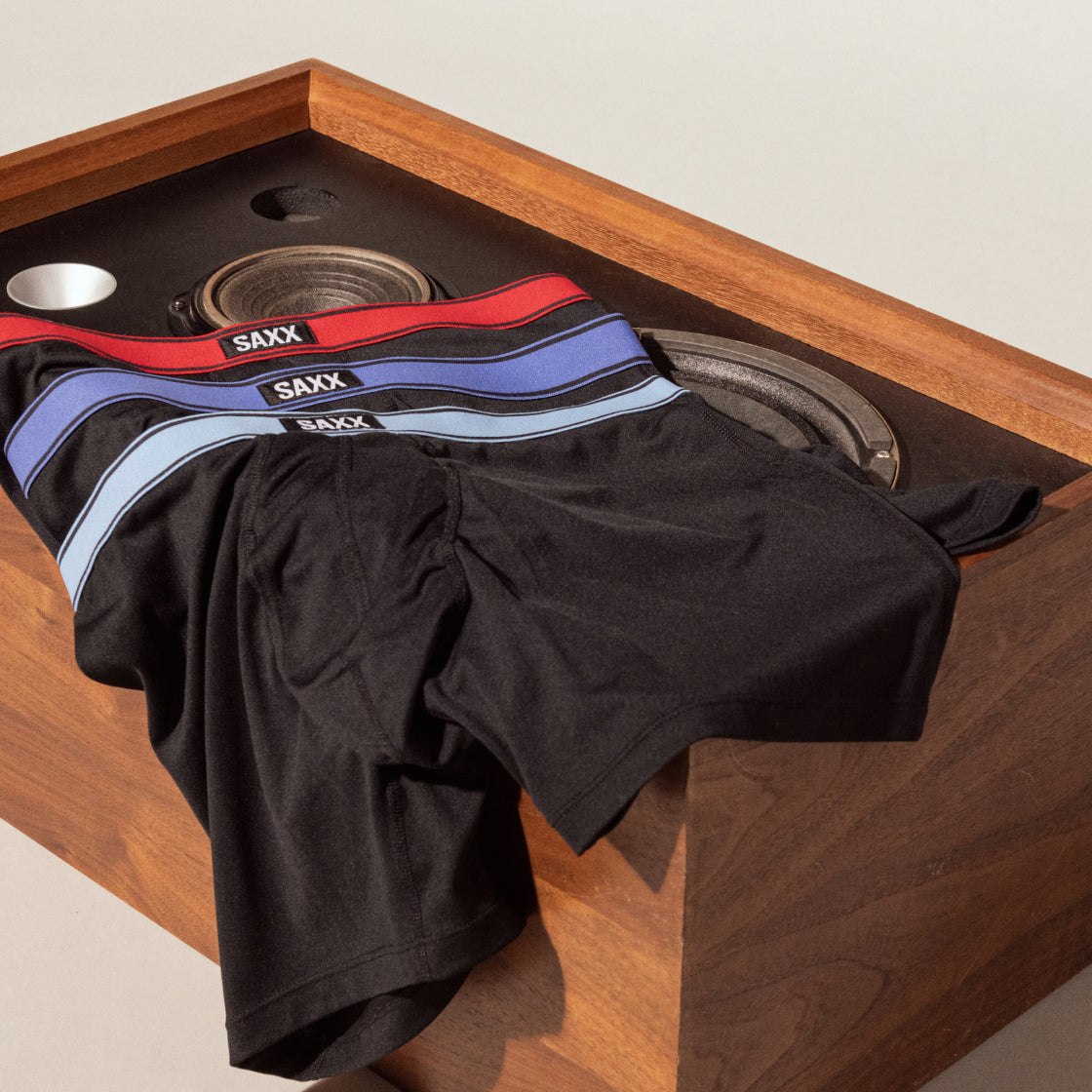 Three pairs of black boxer briefs with waistbands in different colors draped over a wooden speaker
