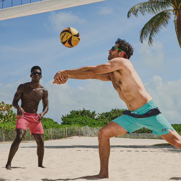 Two men wearing turquoise and pink 2N1 Swim Shorts while playing beach volleyball