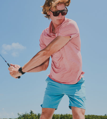 A golfer wearing a pink polo and blue shorts