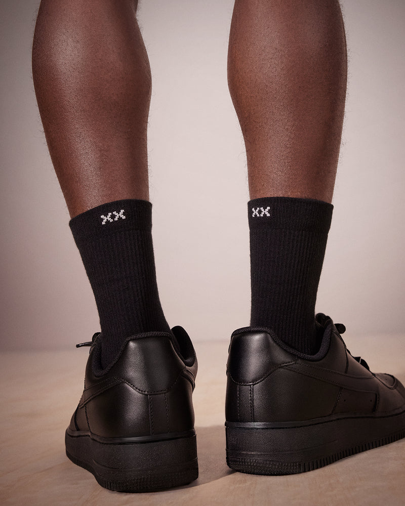 Seen from the rear, a person's lower legs wearing black crew socks and black sneakers.