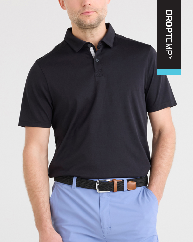 Closeup of man wearing black SAXX DropTemp® Cooling Dry Polo, hand in pocket, in front of neutral backdrop.