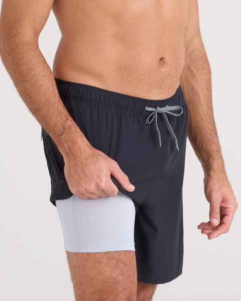 Person wearing black swim shorts with a white patch on a light gray background