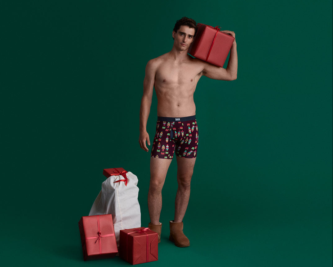 Man wearing patterned underwear holding red gifts against a green background