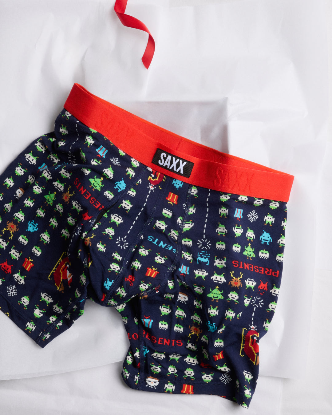 Pair of navy boxer briefs with colorful patterns and red waistband on a white background, featuring the SAXX brand.