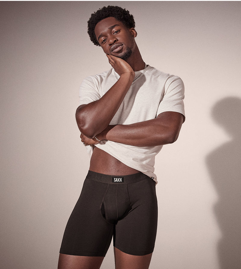 Man wearing a white t-shirt and black underwear with 'SAAX' branding against a neutral background