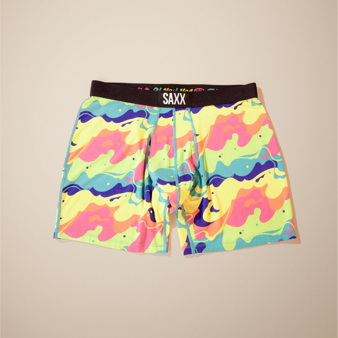 SAXX Boxer Briefs in a bubbled wave pattern in yellow, orange, pink, blue, and seafoam green, laid out over neutral backdrop.