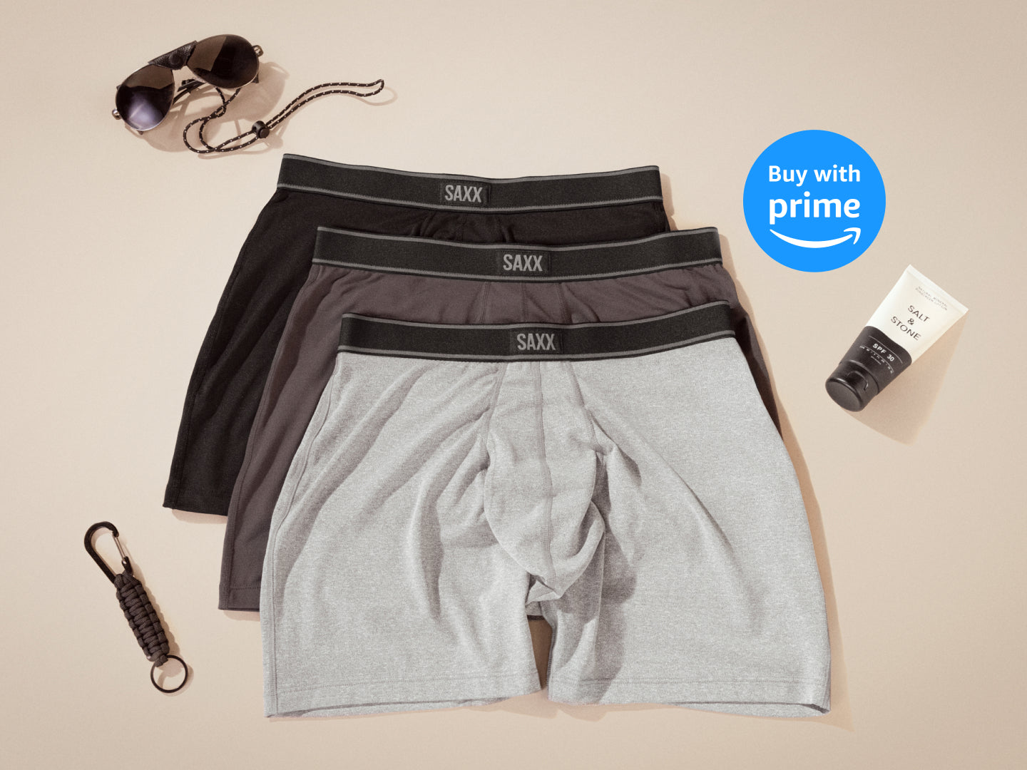 Three pairs of SAXX Boxer Briefs in light grey, dark grey, and black, laid out over neutral backdrop. ‘Buy with Prime’ sticker.