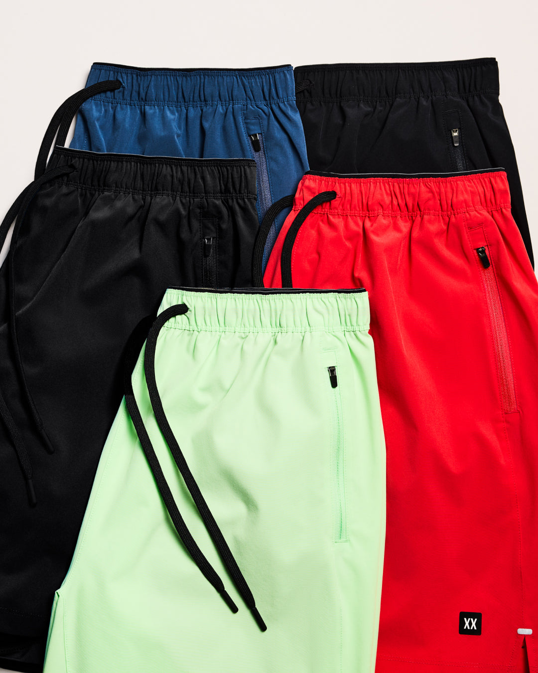 Four pairs of pants in black, blue, green, and red on a light gray background.