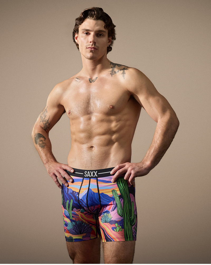 Man wearing colorful SAXX underwear with a desert pattern on a beige background