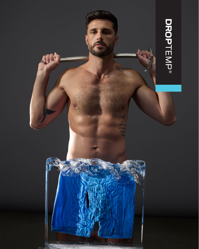 A shirtless male model holds a metal bar over his shoulders while wearing bright blue swim trunks that are frozen in clear ice. The background is dark gray, and a vertical black brand panel on the right reads DROPTEMP with a blue accent bar.