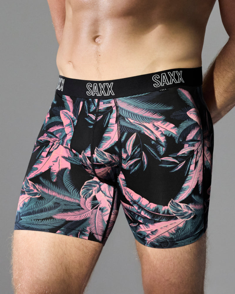 Men's boxer briefs with a black base and a pink and teal tropical leaf pattern, featuring a black elastic waistband with the brand name 'SAXX' printed in white.