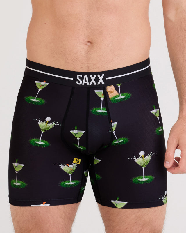 Model wearing black boxer briefs with a golf cocktail pattern and SAXX branding on a white background
