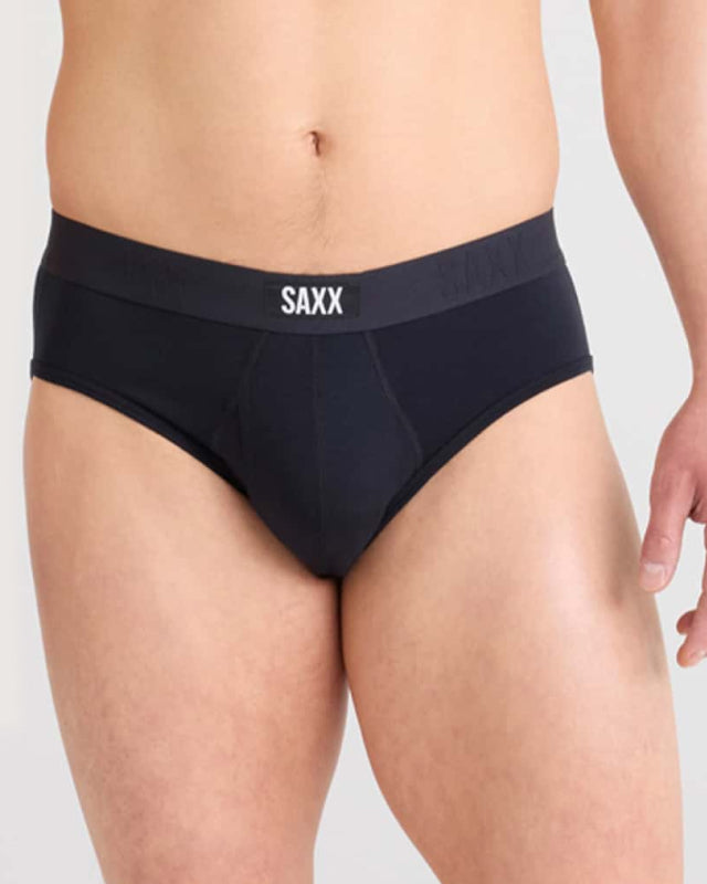 Model wearing black SAXX briefs on a plain background