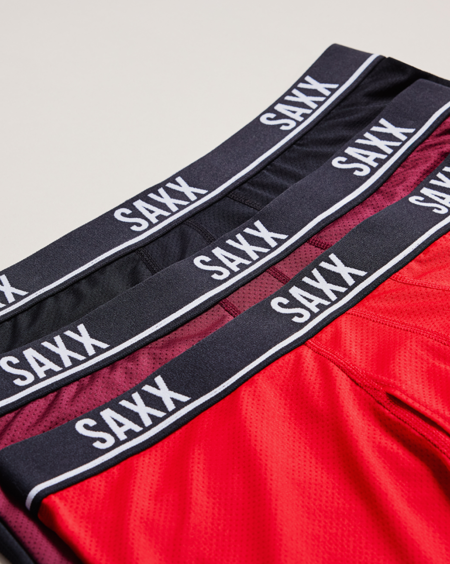 Three pairs of SAXX underwear stacked, in two shades of red and black
