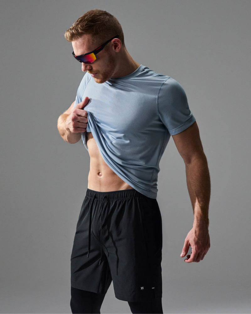 A man wearing a light blue athletic t-shirt and black athletic shorts, posing against a solid gray studio background.