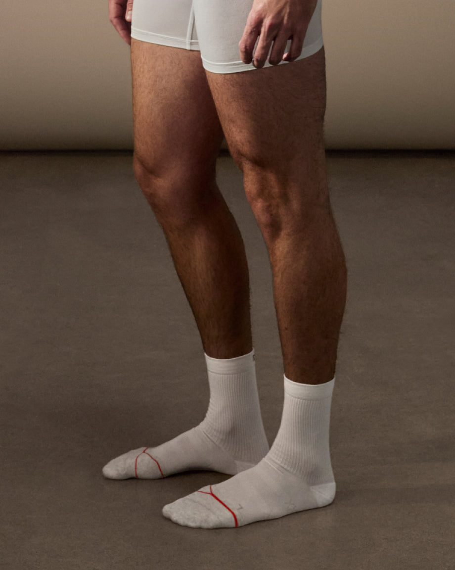 Person wearing white socks with red accents on a brown floor.