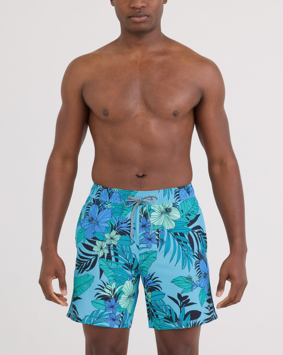 Man wearing blue floral SAXX swim shorts on a plain background