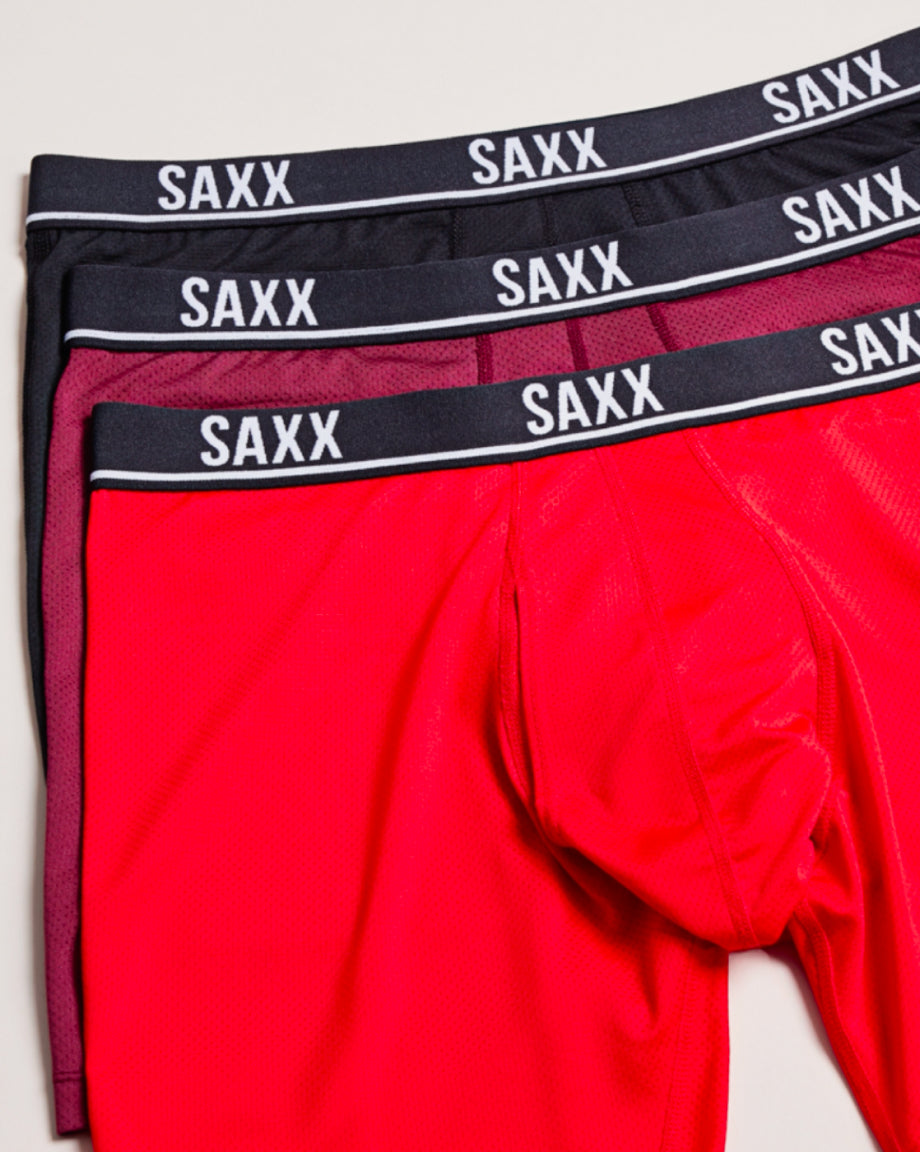Three pairs of SAXX underwear stacked, in two shades of red and black