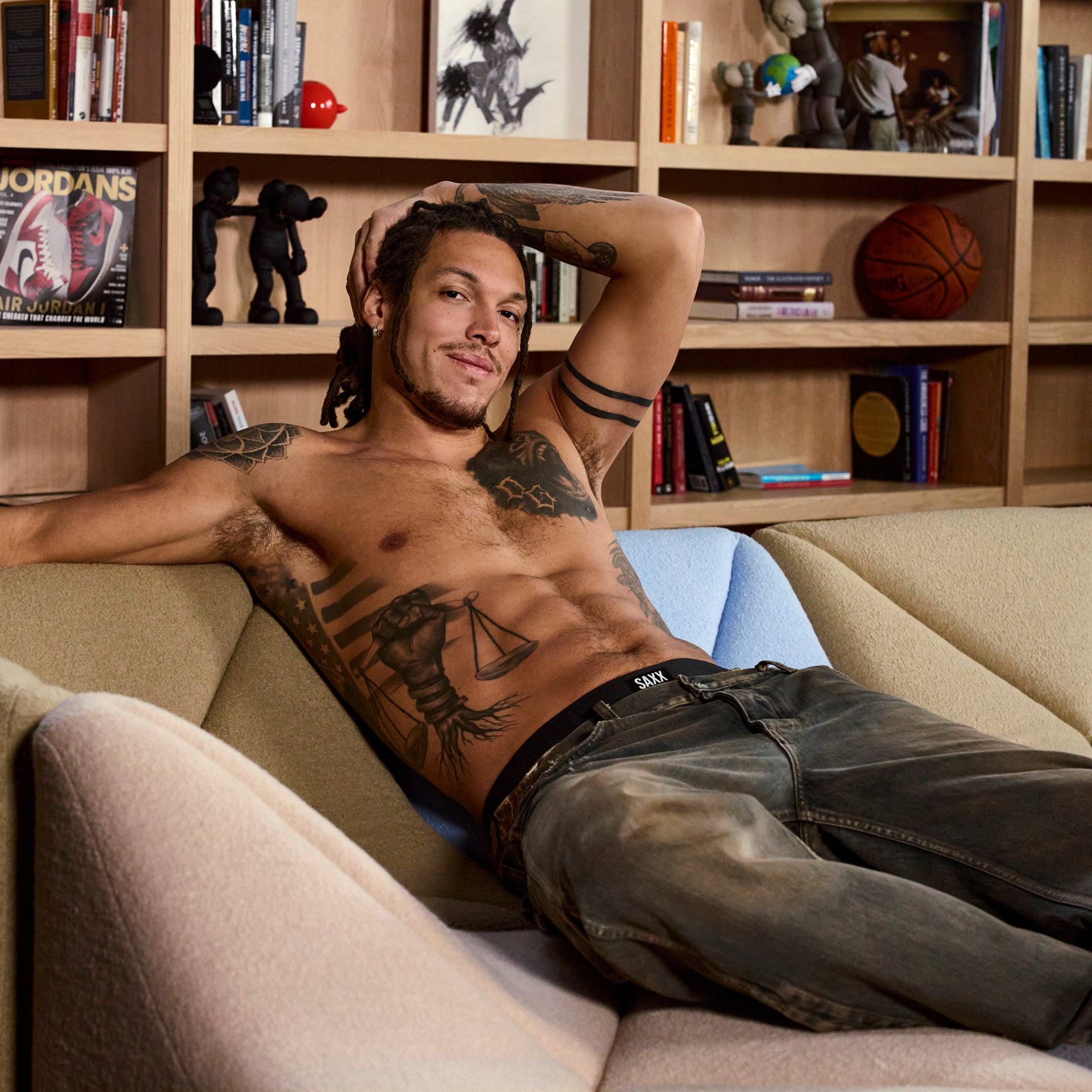 Pro Basketball Player and SAXX Gamechanger Aaron Gordon lying on a couch in a room with bookshelves and sports memorabilia.