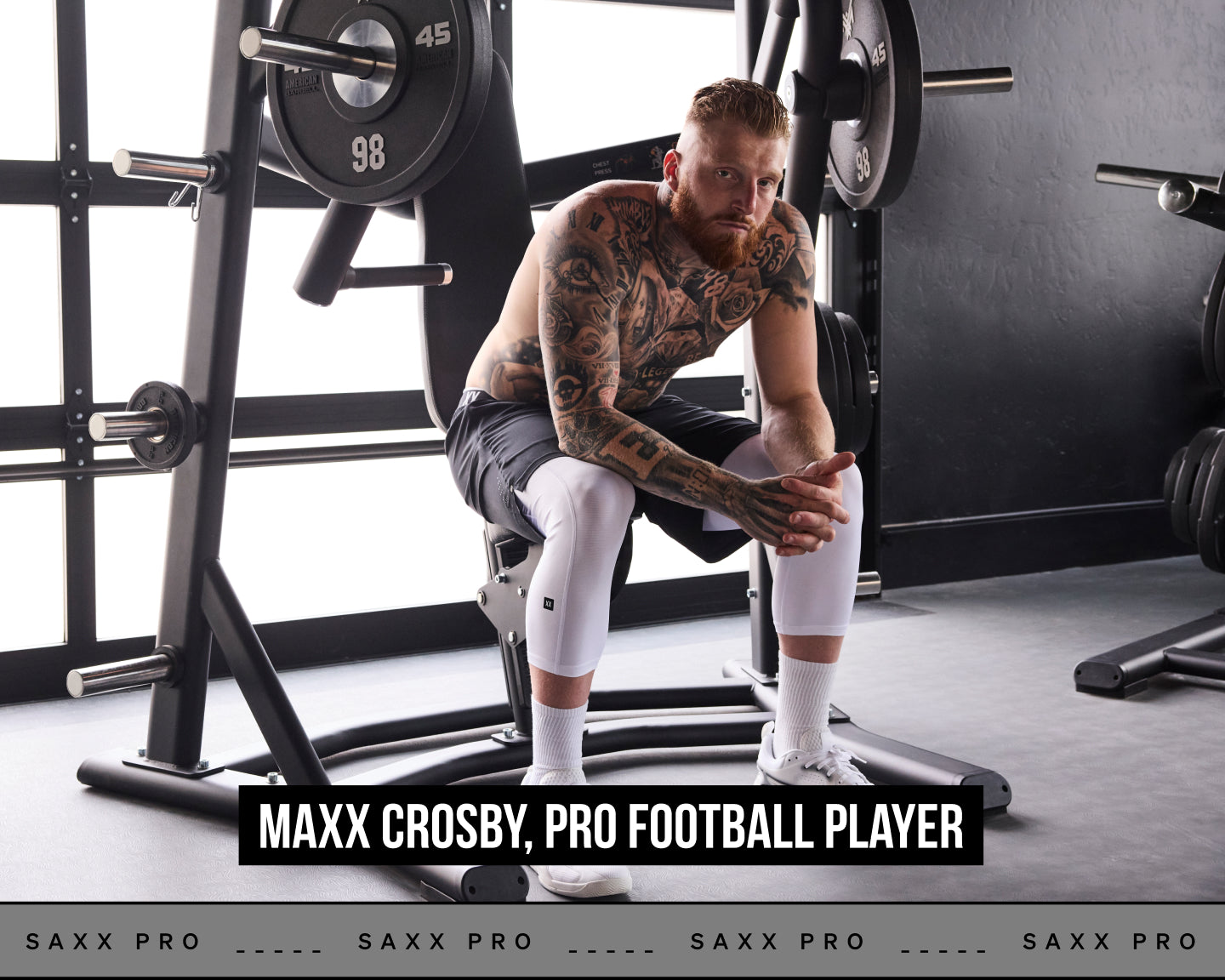 Pro Football player Maxx Crosby sits on a weight bench in a gym setting, wearing a black Saxx Pro football jersey, black shorts, white knee sleeves, white socks, and white sneakers. A text banner at the bottom reads 'MAXX CROSBY, PRO FOOTBALL PLAYER'.